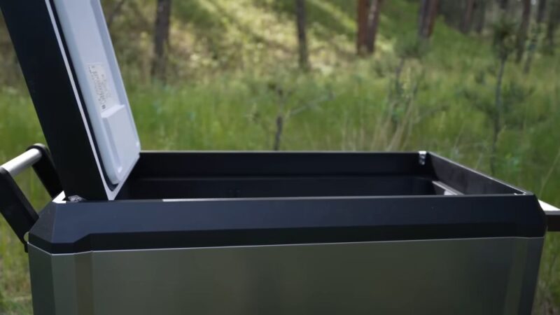 Portable electric car cooler with open lid placed outdoors during camping