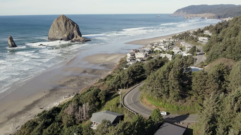 A scenic view of the Oregon Coast shows waves, sandy beaches, and Haystack Rock near a small coastal town