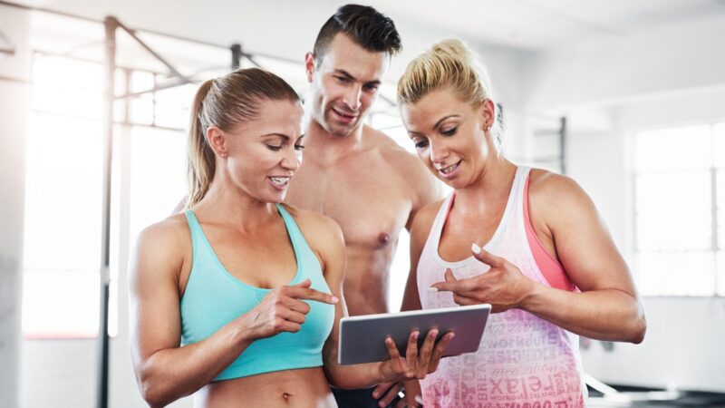 Three gym members review class data on a tablet after a workout
