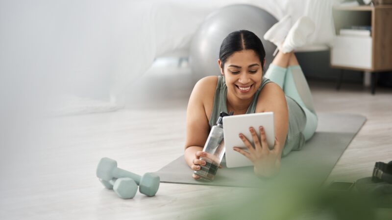 A woman follows a hybrid fitness class on a tablet at home