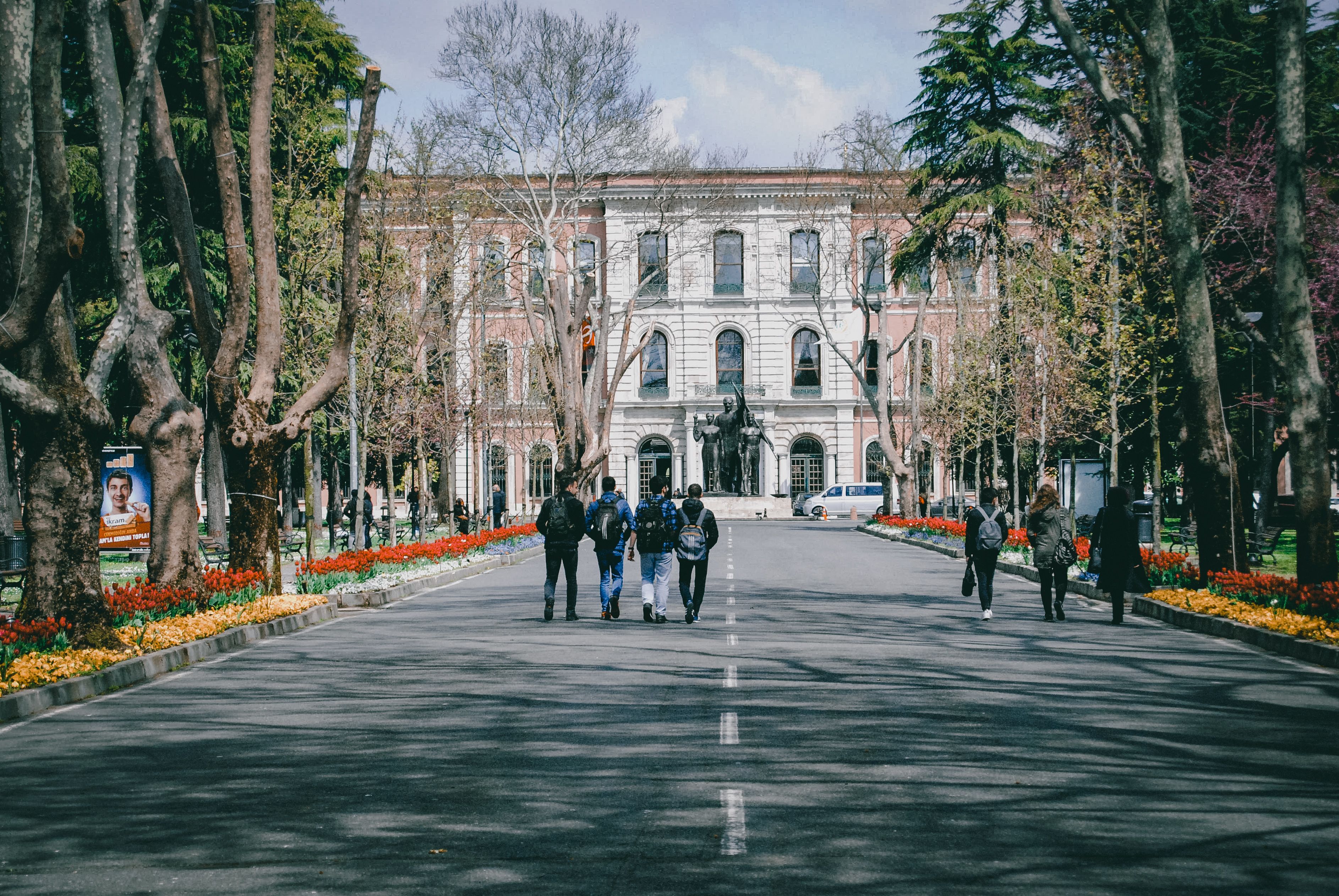 Students walking through a tree-lined university campus with spring flowers, showing how outdoor design supports daily campus life.